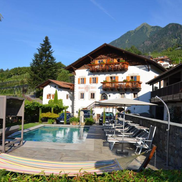 Beheizter Salzwasserpool mit Liegestühlen und Hängematte am Mayerhof in Kuens bei Meran – traditionelles Südtiroler Bauernhaus mit Bergpanorama der Texelgruppe im Hintergrund