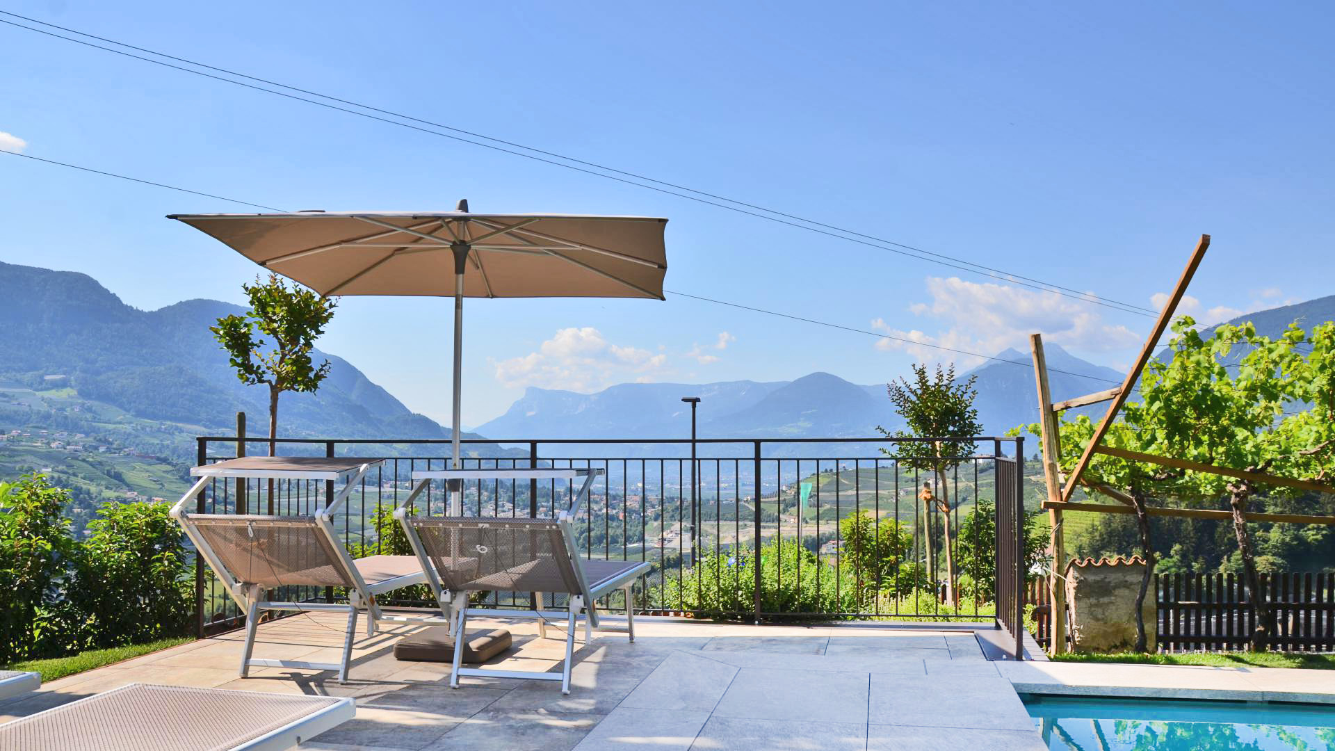 Sonnenterrasse am Pool des Mayerhofs in Kuens mit Liegestühlen und Sonnenschirm &ndash; weiter Ausblick auf Meran und das Etschtal